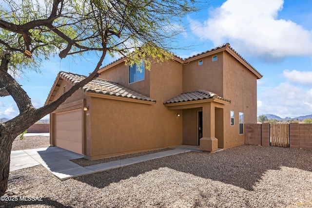 mediterranean / spanish-style house featuring an attached garage, fence, a tile roof, concrete driveway, and stucco siding