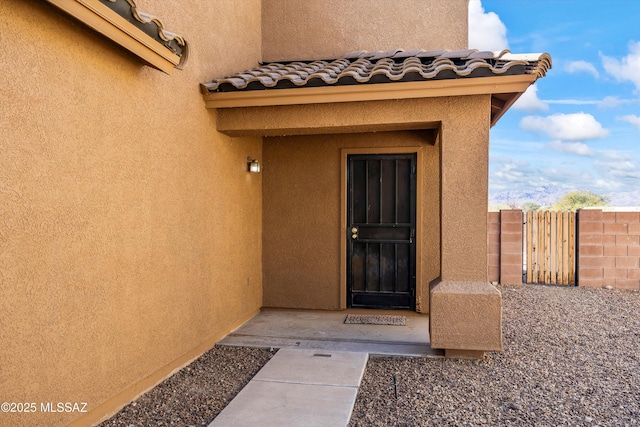 entrance to property with a tiled roof, fence, and stucco siding