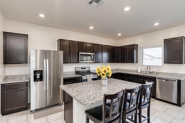 kitchen featuring a breakfast bar, visible vents, appliances with stainless steel finishes, a kitchen island, and a sink