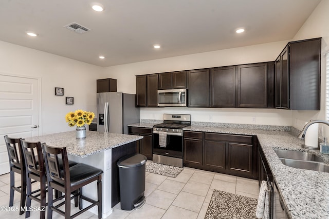 kitchen featuring light stone counters, a center island, a breakfast bar area, stainless steel appliances, and a sink