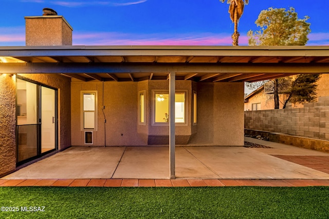 9990 E Mary Dr, Tucson, AZ 85730 - back of house at dusk with fence, a patio area, a chimney, and stucco siding