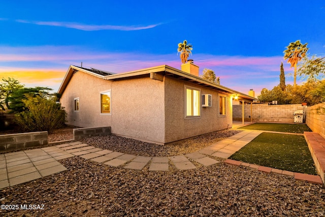 9990 E Mary Dr, Tucson, AZ 85730 - property exterior at dusk featuring a chimney, a fenced backyard, a wall mounted AC, solar panels, and stucco siding
