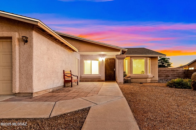 9990 E Mary Dr, Tucson, AZ 85730 - exterior entry at dusk with fence, roof with shingles, and stucco siding
