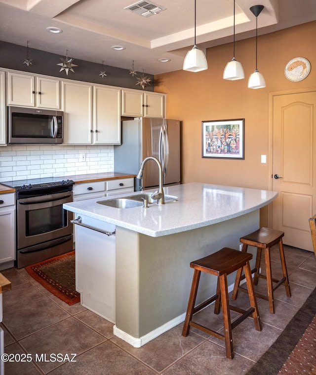 kitchen with a tray ceiling, visible vents, appliances with stainless steel finishes, and a sink