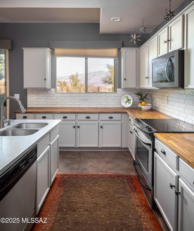 kitchen featuring tasteful backsplash, wood counters, appliances with stainless steel finishes, dark tile patterned floors, and a sink