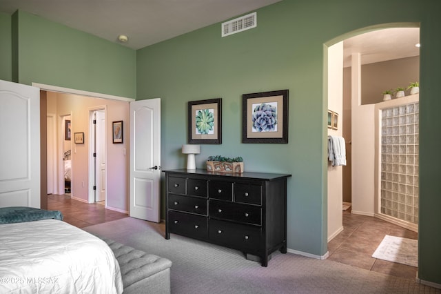 bedroom with arched walkways, visible vents, baseboards, tile patterned floors, and carpet