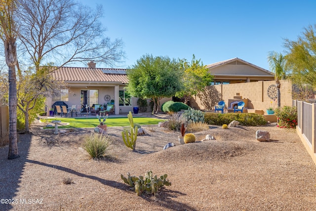 back of house with a tile roof, a chimney, fence, a patio area, and roof mounted solar panels