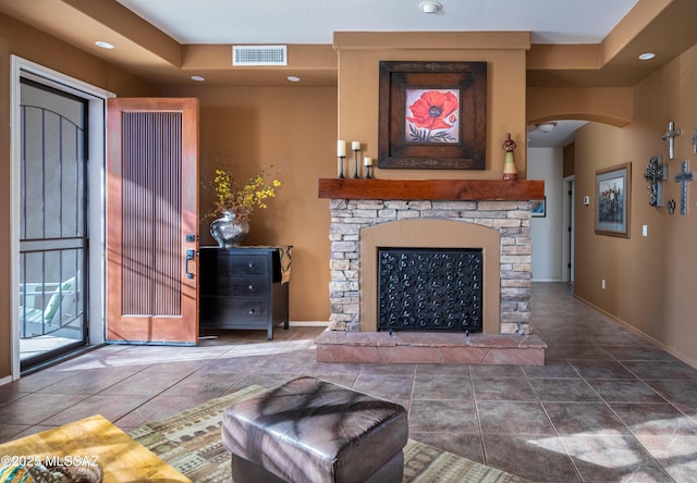 living area with baseboards, visible vents, arched walkways, tile patterned floors, and a stone fireplace