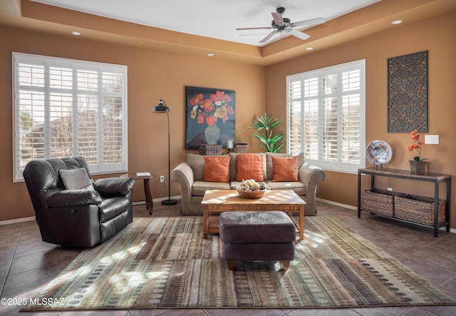 living area featuring a tray ceiling, recessed lighting, ceiling fan, tile patterned flooring, and baseboards