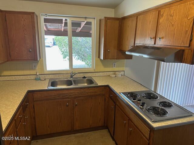 kitchen featuring light countertops, brown cabinetry, a sink, electric stovetop, and under cabinet range hood