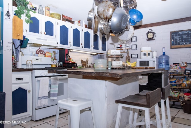 kitchen with white appliances, dark countertops, light tile patterned flooring, and under cabinet range hood