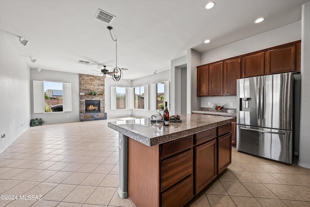 kitchen with light tile patterned floors, tile countertops, a stone fireplace, and stainless steel refrigerator with ice dispenser