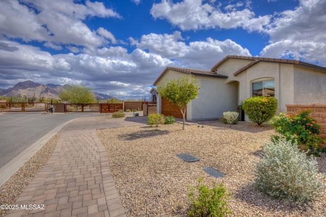 view of side of home featuring a gate, fence, an attached garage, stucco siding, and a mountain view