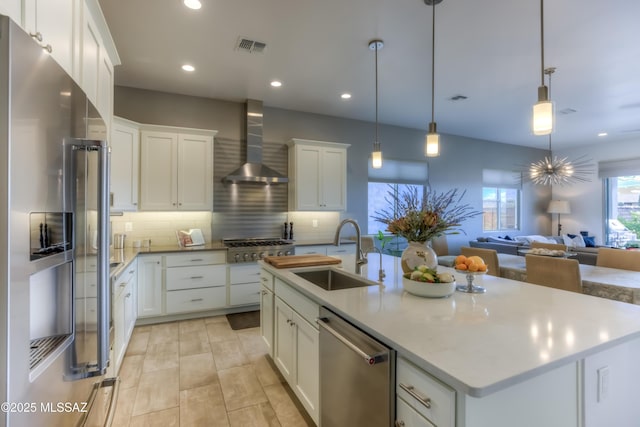 kitchen featuring a sink, appliances with stainless steel finishes, white cabinets, wall chimney range hood, and decorative backsplash