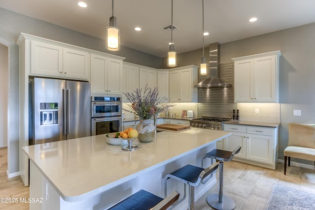 kitchen featuring backsplash, a kitchen island, wall chimney range hood, appliances with stainless steel finishes, and white cabinets