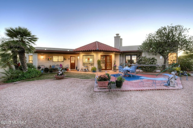 rear view of house with a chimney, a tiled roof, french doors, a patio area, and stucco siding