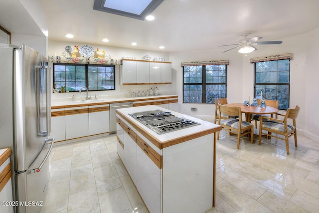 kitchen featuring white cabinets, a kitchen island, stainless steel appliances, light countertops, and a sink