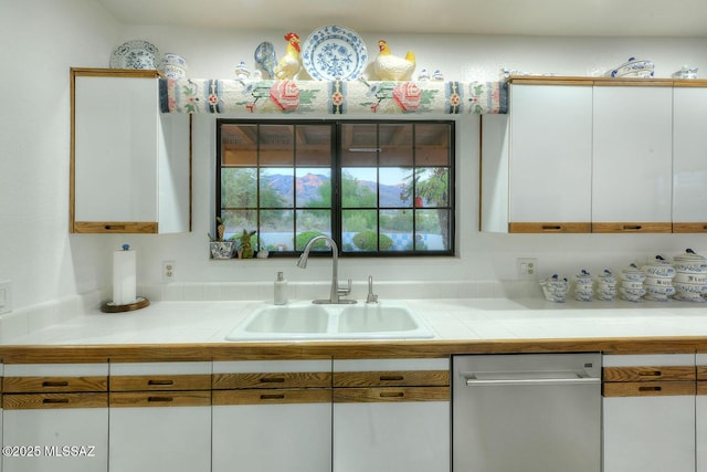 kitchen with tile counters, white cabinetry, and a sink