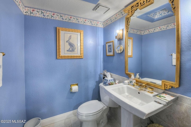 half bathroom featuring a sink, tile patterned flooring, toilet, and baseboards