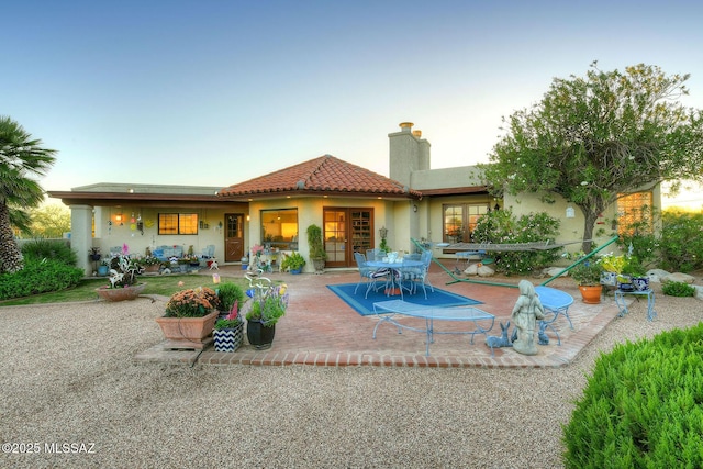 rear view of property with stucco siding, a chimney, a tiled roof, a patio area, and outdoor dining space