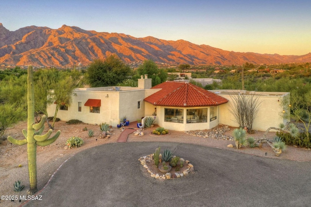 view of front facade with driveway, a tile roof, a chimney, a mountain view, and stucco siding