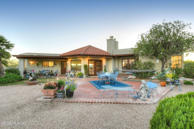 rear view of house featuring a patio area, a tiled roof, a chimney, and stucco siding