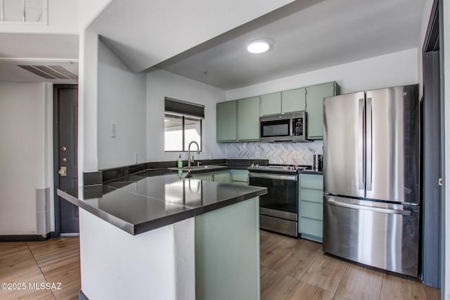 kitchen with green cabinetry, dark countertops, a peninsula, stainless steel appliances, and a sink