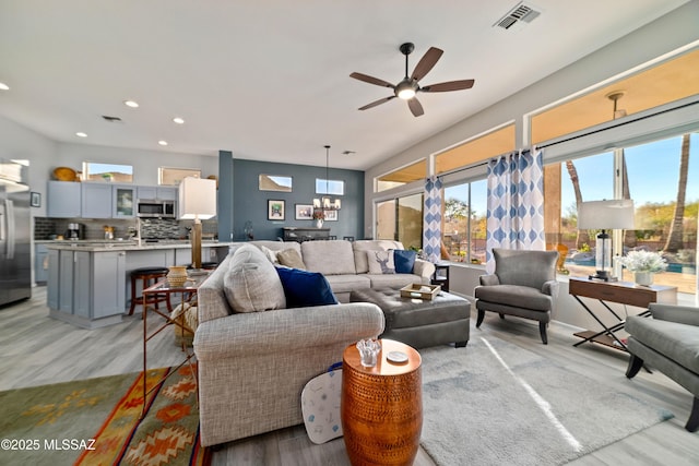 living room featuring light wood-style flooring, ceiling fan with notable chandelier, visible vents, and recessed lighting