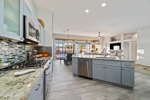 kitchen with backsplash, gray cabinetry, appliances with stainless steel finishes, open floor plan, and a sink