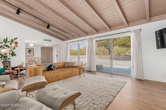 living area with light wood-style flooring, a stone fireplace, visible vents, and lofted ceiling with beams