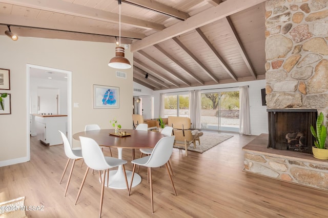 dining area with light wood finished floors, lofted ceiling with beams, wood ceiling, rail lighting, and a stone fireplace