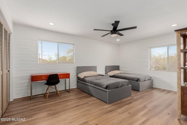 bedroom with brick wall, light wood-style flooring, and recessed lighting