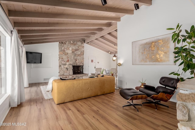 living area with lofted ceiling with beams, light wood-style floors, plenty of natural light, and a stone fireplace