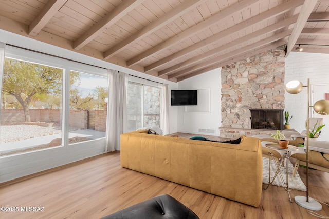 living room featuring lofted ceiling with beams, light wood finished floors, visible vents, and a stone fireplace