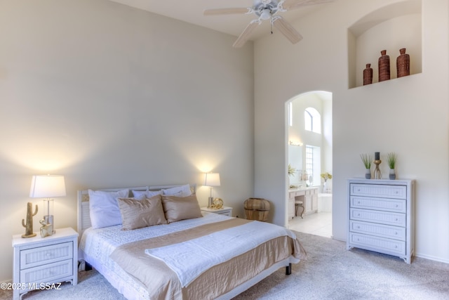 carpeted bedroom featuring arched walkways, a ceiling fan, ensuite bath, and a towering ceiling