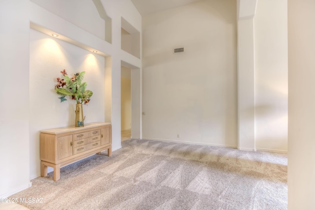 spare room with light carpet, visible vents, baseboards, and a towering ceiling