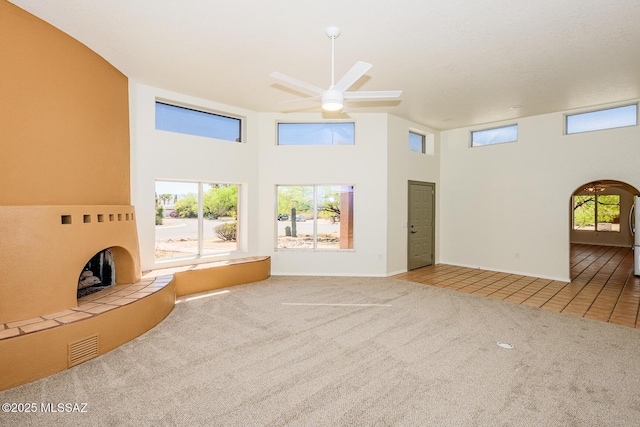 unfurnished living room with carpet flooring, a towering ceiling, baseboards, tile patterned flooring, and ceiling fan