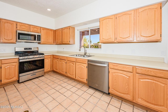 kitchen with stainless steel appliances, a sink, light tile patterned flooring, light brown cabinets, and light countertops