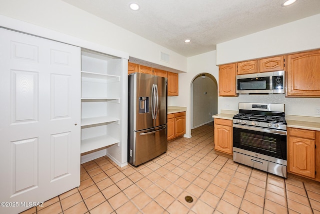 kitchen with light tile patterned floors, open shelves, stainless steel appliances, light countertops, and arched walkways