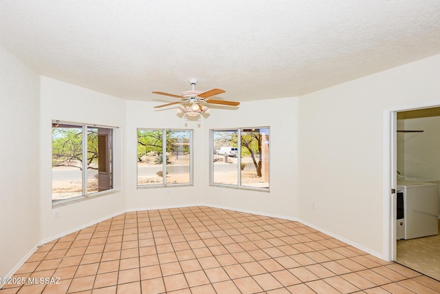 empty room with washer / dryer, a ceiling fan, and light tile patterned floors
