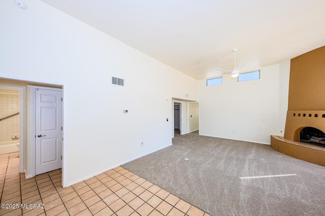 unfurnished living room featuring light carpet, baseboards, visible vents, a ceiling fan, and a high ceiling