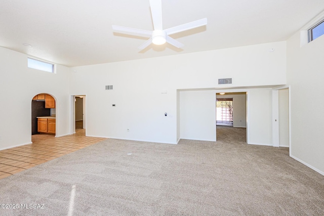 spare room featuring light colored carpet, ceiling fan, a high ceiling, and visible vents
