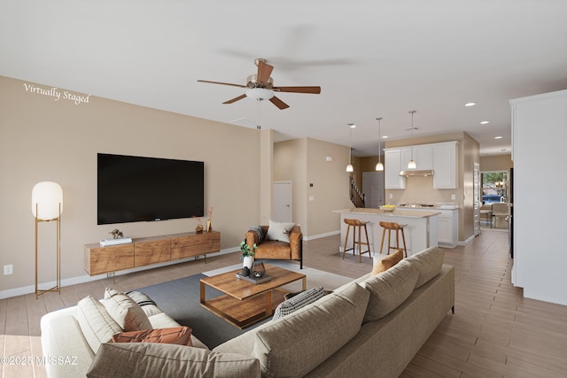 living area with light wood-type flooring, ceiling fan, baseboards, and recessed lighting