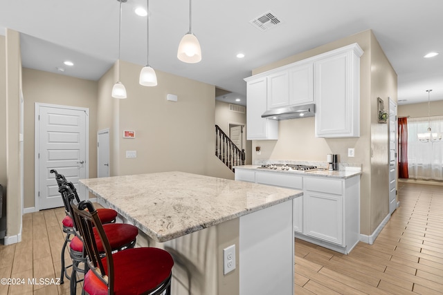 kitchen featuring pendant lighting, under cabinet range hood, white cabinetry, and a center island