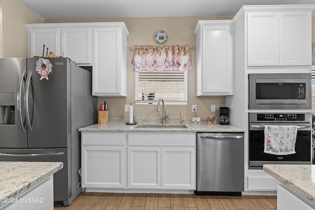 kitchen featuring light wood finished floors, white cabinets, light stone countertops, stainless steel appliances, and a sink