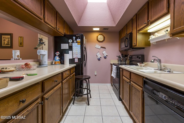 kitchen with a tray ceiling, brown cabinets, light countertops, light tile patterned flooring, and black appliances