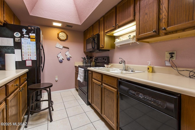 kitchen with light tile patterned floors, a sink, light countertops, black appliances, and brown cabinetry