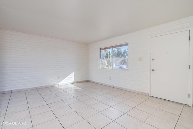 spare room featuring light tile patterned floors and brick wall