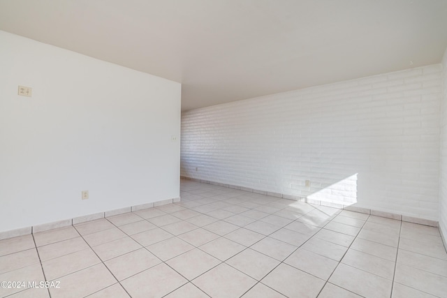 spare room featuring brick wall, baseboards, and light tile patterned flooring