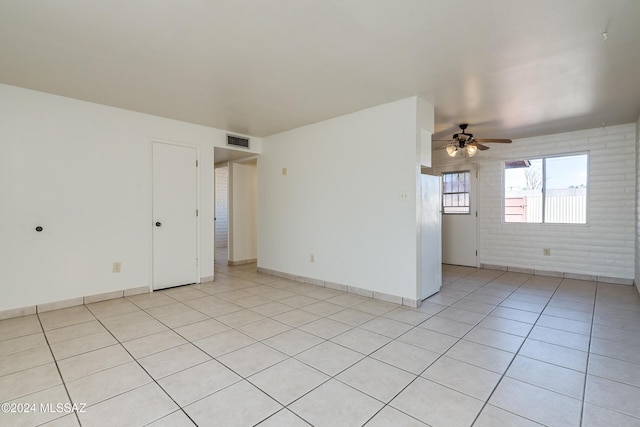 spare room featuring light tile patterned floors, visible vents, a ceiling fan, brick wall, and baseboards